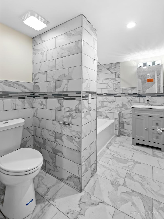 bathroom featuring a tub to relax in, vanity, tile walls, and toilet