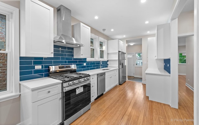 kitchen featuring white cabinets, wall chimney exhaust hood, backsplash, and stainless steel appliances