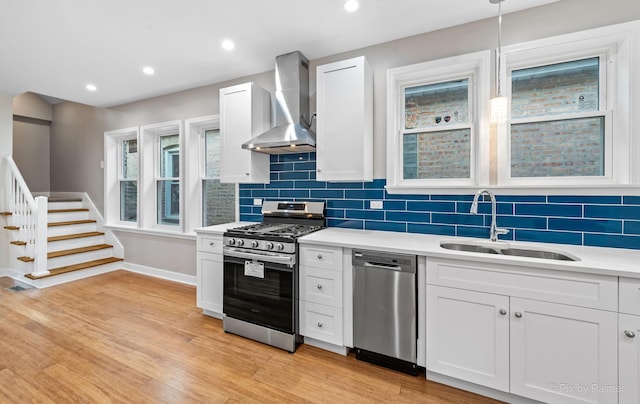 kitchen featuring white cabinets, sink, stainless steel appliances, and wall chimney range hood