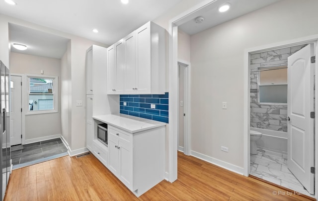 kitchen featuring stainless steel microwave, white cabinetry, backsplash, and light hardwood / wood-style flooring