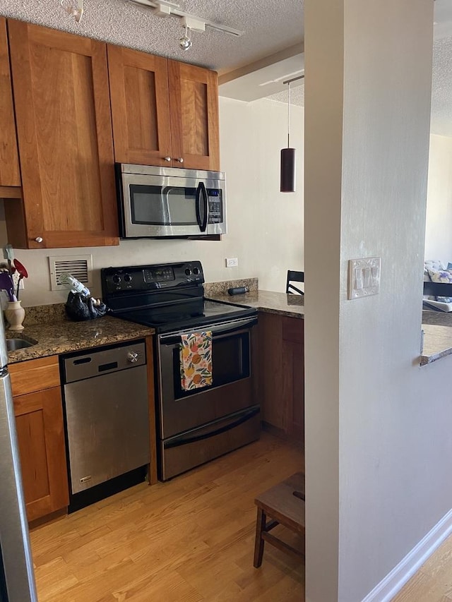 kitchen with a textured ceiling, stainless steel appliances, decorative light fixtures, light hardwood / wood-style flooring, and dark stone countertops