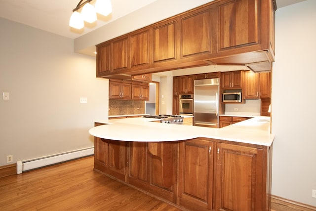 kitchen featuring kitchen peninsula, decorative backsplash, light wood-type flooring, appliances with stainless steel finishes, and a baseboard radiator