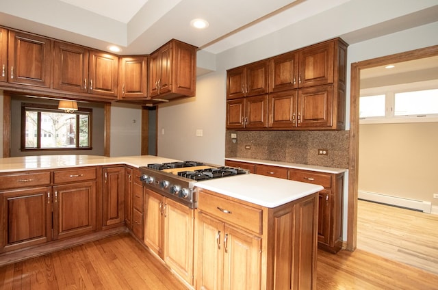 kitchen with baseboard heating, tasteful backsplash, stainless steel gas stovetop, kitchen peninsula, and light hardwood / wood-style flooring