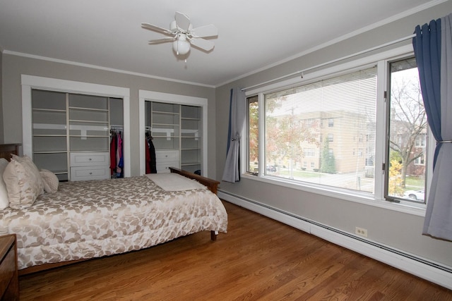 bedroom with two closets, hardwood / wood-style flooring, a baseboard heating unit, ceiling fan, and crown molding