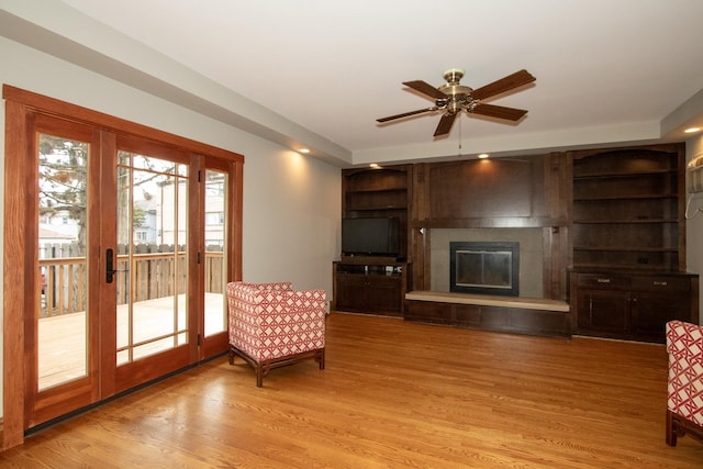 unfurnished living room with built in shelves, french doors, a fireplace, light hardwood / wood-style floors, and ceiling fan