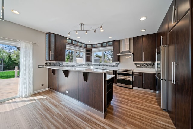 kitchen with appliances with stainless steel finishes, plenty of natural light, open shelves, and wall chimney exhaust hood