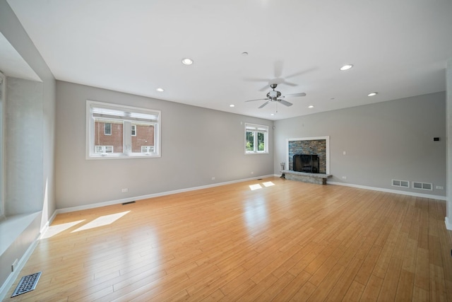 unfurnished living room featuring light wood-style flooring, a ceiling fan, a stone fireplace, and visible vents