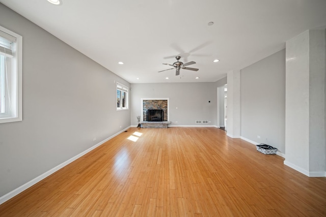 unfurnished living room with light wood-style floors, baseboards, a ceiling fan, and a stone fireplace