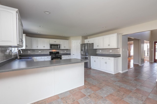 kitchen with kitchen peninsula, tasteful backsplash, stainless steel appliances, sink, and white cabinets