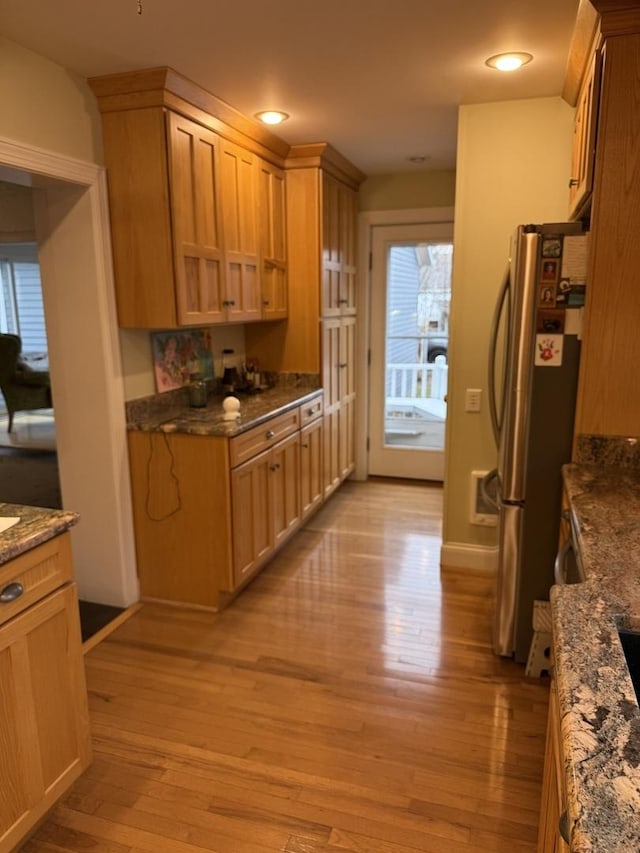 kitchen with stainless steel refrigerator, light hardwood / wood-style flooring, and dark stone counters