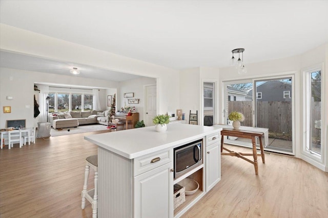 kitchen with a kitchen island, stainless steel microwave, light hardwood / wood-style flooring, white cabinetry, and hanging light fixtures