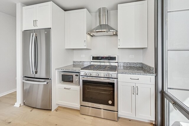 kitchen with appliances with stainless steel finishes, sink, white cabinets, light stone countertops, and wall chimney range hood