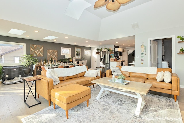 living room featuring a skylight, ceiling fan, and light hardwood / wood-style floors