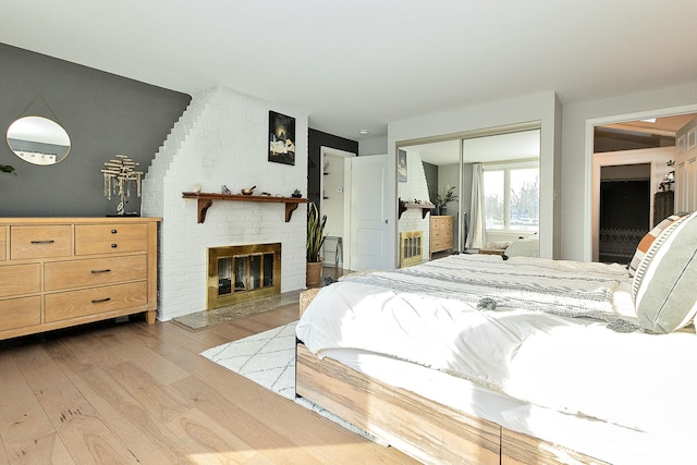 bedroom with a brick fireplace, a closet, and light wood-type flooring