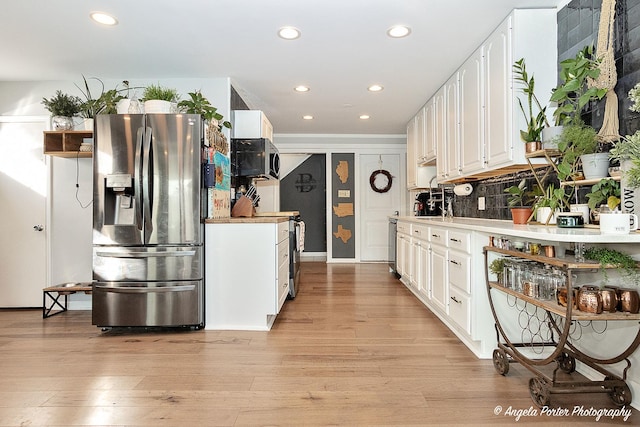 kitchen with tasteful backsplash, white cabinetry, appliances with stainless steel finishes, and light hardwood / wood-style flooring