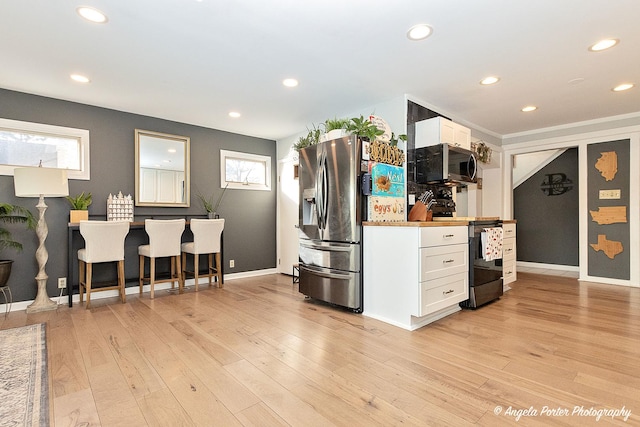 kitchen with a kitchen bar, white cabinets, light wood-type flooring, and appliances with stainless steel finishes