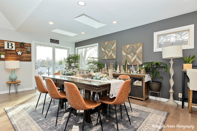 dining room with hardwood / wood-style floors and vaulted ceiling with skylight