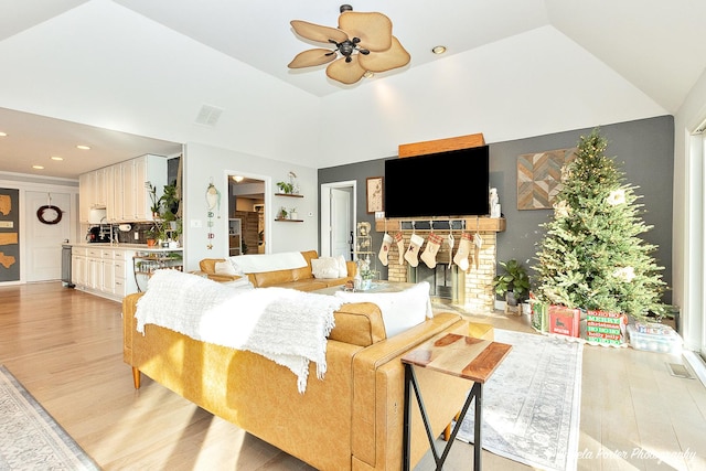 living room with ceiling fan, light hardwood / wood-style floors, lofted ceiling, and a brick fireplace