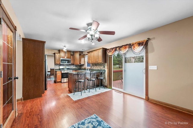 kitchen featuring a kitchen breakfast bar, backsplash, appliances with stainless steel finishes, ceiling fan, and light hardwood / wood-style floors