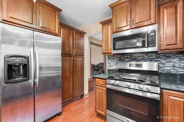 kitchen with backsplash, stainless steel appliances, dark stone counters, and light hardwood / wood-style flooring