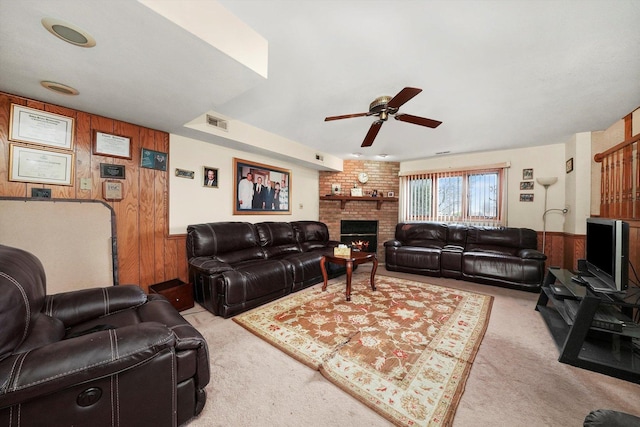 living room featuring light carpet, ceiling fan, a fireplace, and wood walls