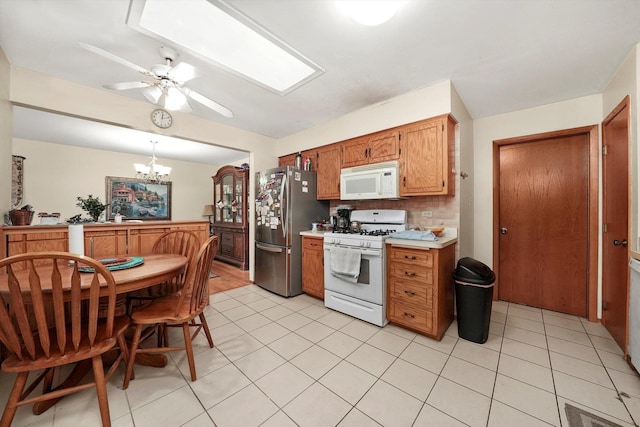 kitchen featuring hanging light fixtures, white appliances, decorative backsplash, light tile patterned flooring, and ceiling fan with notable chandelier