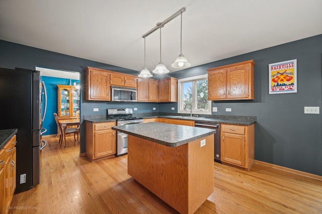 kitchen with decorative light fixtures, sink, light wood-type flooring, a center island, and stainless steel appliances