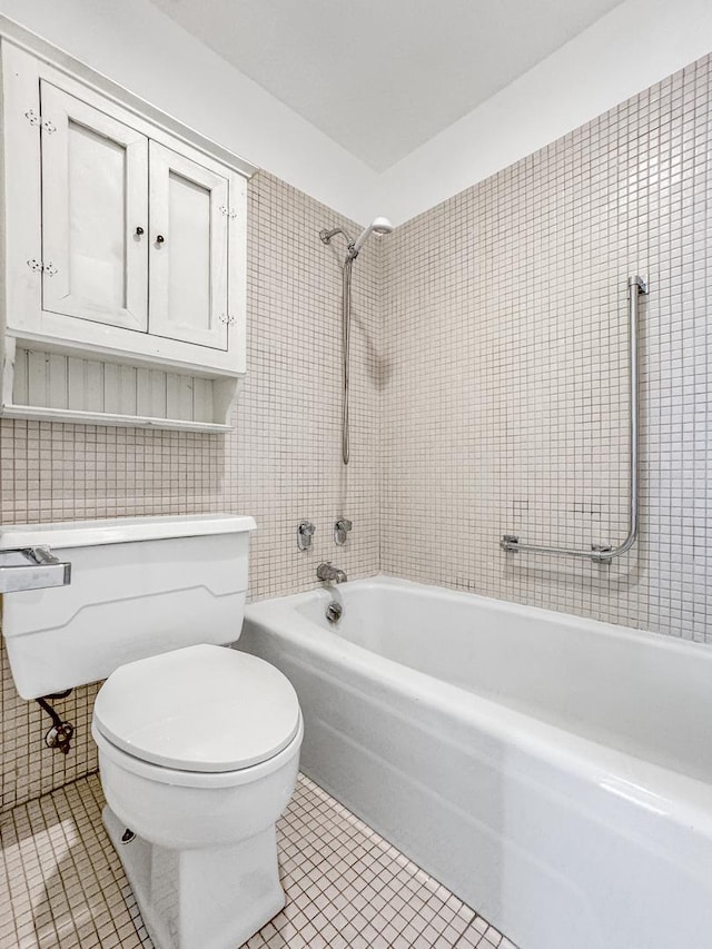 bathroom featuring toilet, tiled shower / bath combo, tile patterned floors, and tile walls