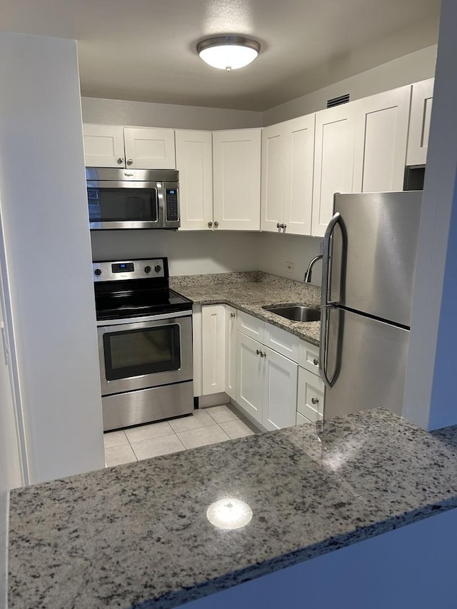 kitchen featuring light stone countertops, sink, light tile patterned flooring, white cabinets, and appliances with stainless steel finishes