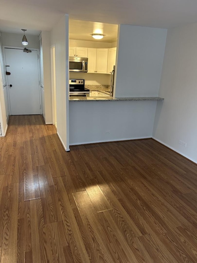 kitchen with kitchen peninsula, light stone countertops, appliances with stainless steel finishes, dark hardwood / wood-style flooring, and white cabinetry