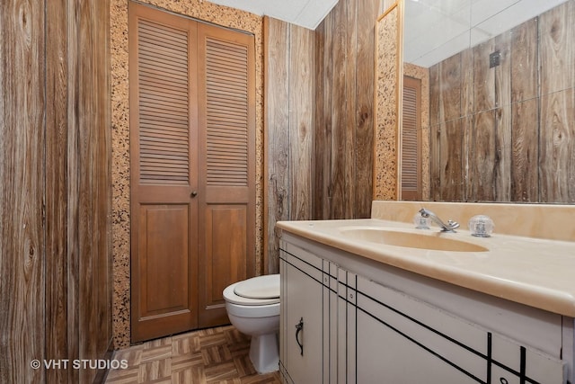 bathroom featuring vanity, toilet, parquet floors, and wooden walls