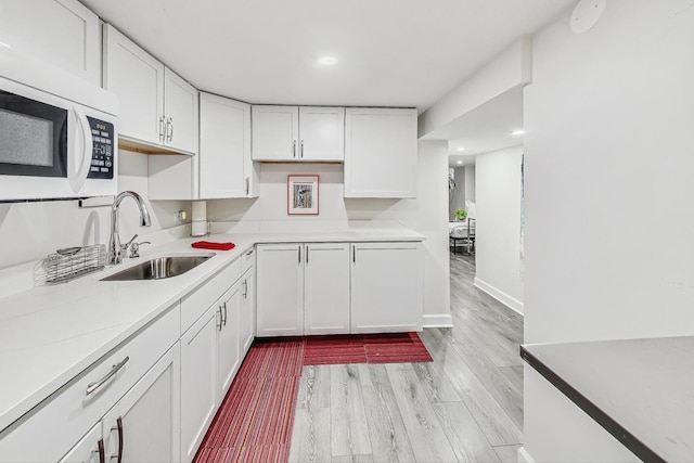 kitchen with white cabinets, light wood-type flooring, light stone counters, and sink