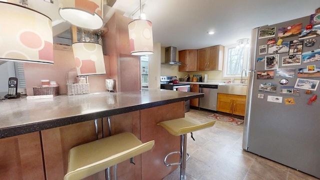 kitchen with sink, wall chimney exhaust hood, appliances with stainless steel finishes, decorative light fixtures, and kitchen peninsula