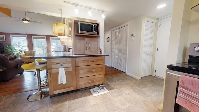 kitchen featuring ceiling fan, rail lighting, hanging light fixtures, a kitchen breakfast bar, and stainless steel range oven