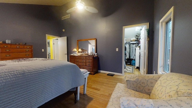 bedroom featuring ceiling fan, light hardwood / wood-style flooring, a towering ceiling, a walk in closet, and a closet