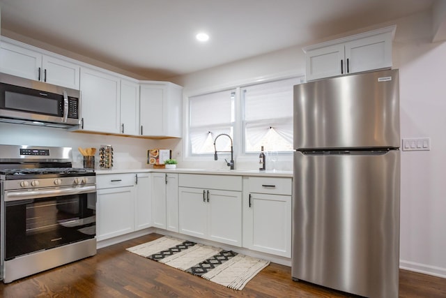 kitchen with appliances with stainless steel finishes, white cabinetry, dark wood-type flooring, and sink