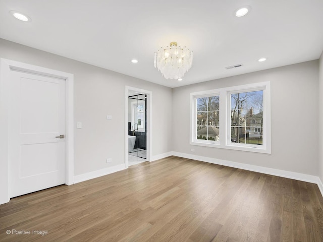 spare room featuring wood-type flooring and a chandelier