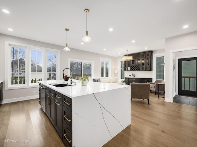 kitchen with light wood-type flooring, a kitchen island with sink, and pendant lighting