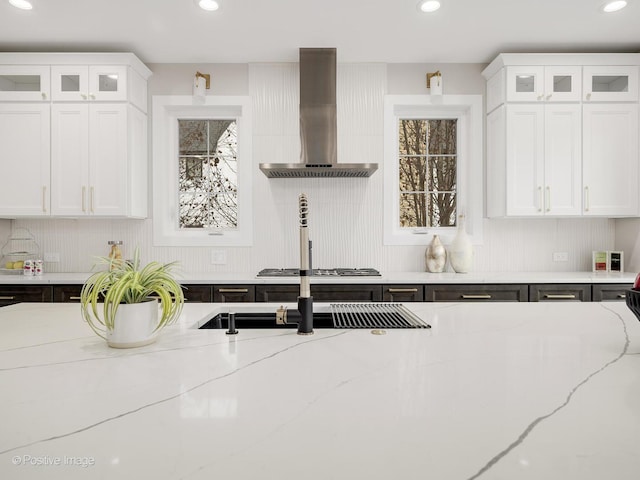 room details featuring wall chimney exhaust hood, white cabinets, gas cooktop, and light stone countertops