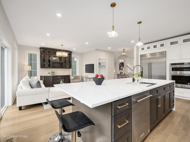 kitchen featuring sink, white cabinets, light wood-type flooring, an island with sink, and stainless steel appliances