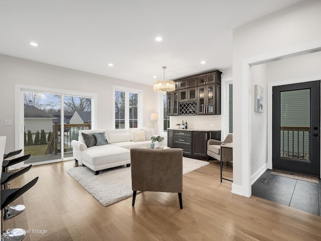 living room with bar, an inviting chandelier, and light hardwood / wood-style floors