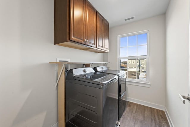 clothes washing area with cabinets, washing machine and clothes dryer, and dark hardwood / wood-style flooring