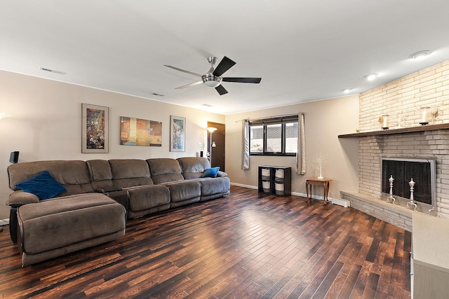 living room featuring ceiling fan, a large fireplace, and dark wood-type flooring