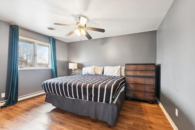 bedroom with ceiling fan, wood-type flooring, and a baseboard heating unit