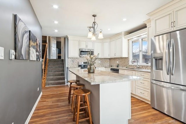 kitchen with light stone countertops, a center island, pendant lighting, appliances with stainless steel finishes, and light wood-type flooring