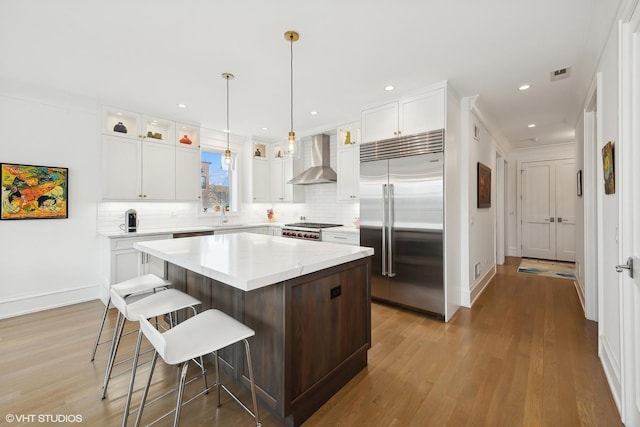 kitchen featuring white cabinetry, a center island, wall chimney range hood, light hardwood / wood-style floors, and appliances with stainless steel finishes