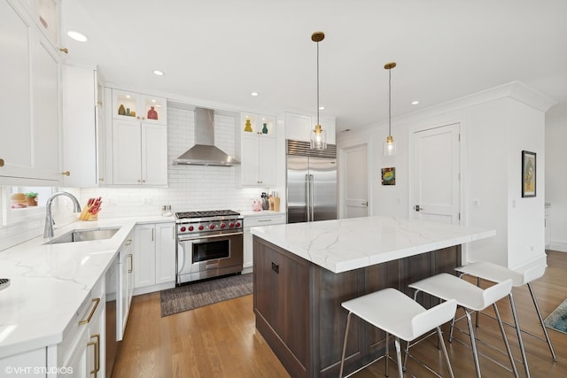 kitchen with premium appliances, sink, wall chimney range hood, white cabinets, and a kitchen island