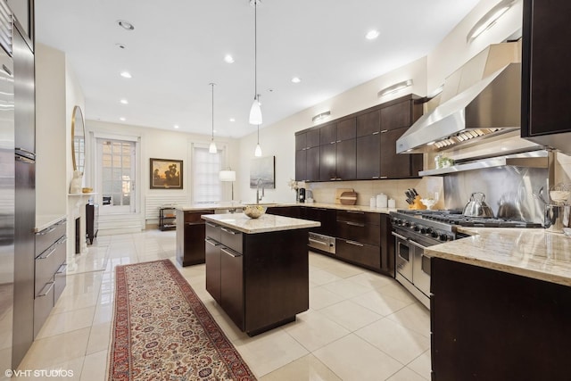 kitchen featuring pendant lighting, double oven range, a center island, dark brown cabinetry, and wall chimney range hood