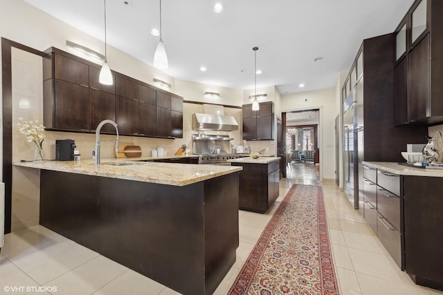 kitchen with sink, decorative light fixtures, dark brown cabinets, kitchen peninsula, and wall chimney range hood