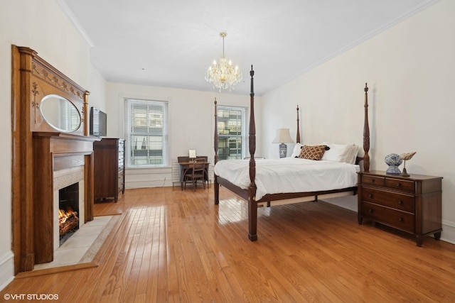 bedroom featuring a tile fireplace, ornamental molding, a notable chandelier, and light wood-type flooring